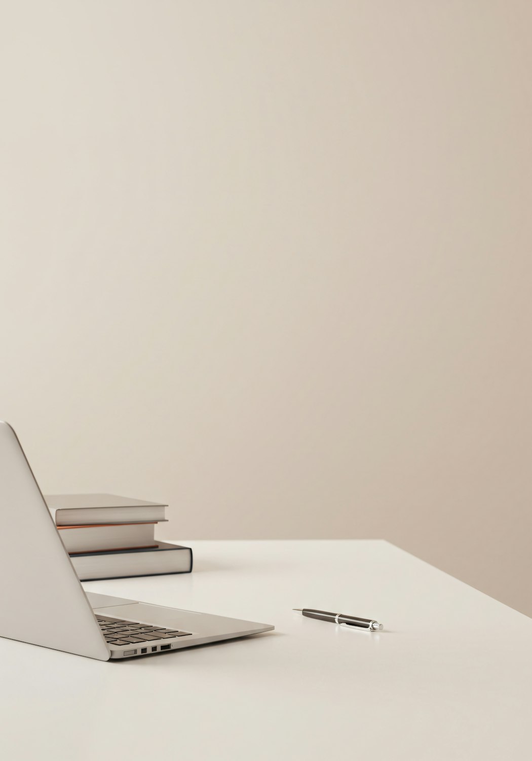 A tidy desk with a laptop, books and a pen